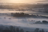 Fototapeta Niebo - Stunning foggy English rural landscape at sunrise in Winter with layers rolling through the fields