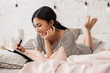 Smiling asian woman laying on couch and writing in book. Close up portrait of relaxing young girl in bedroom. Education and relax concept. Modern bright home interior on background.