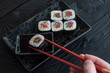 Hand using chopsticks pick. Maki-Sushi, tuna-maki rolls in front of face of young man. Fresh made Sushi set with tuna, cheese and cucumber. Traditional Japanese cuisine.