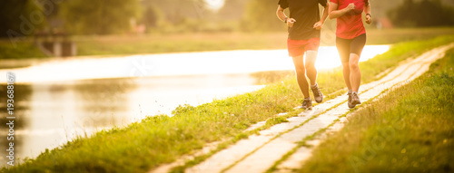 Cuadros en Lienzo Couple running outdoors, at sunset, by a river, staying active and fit