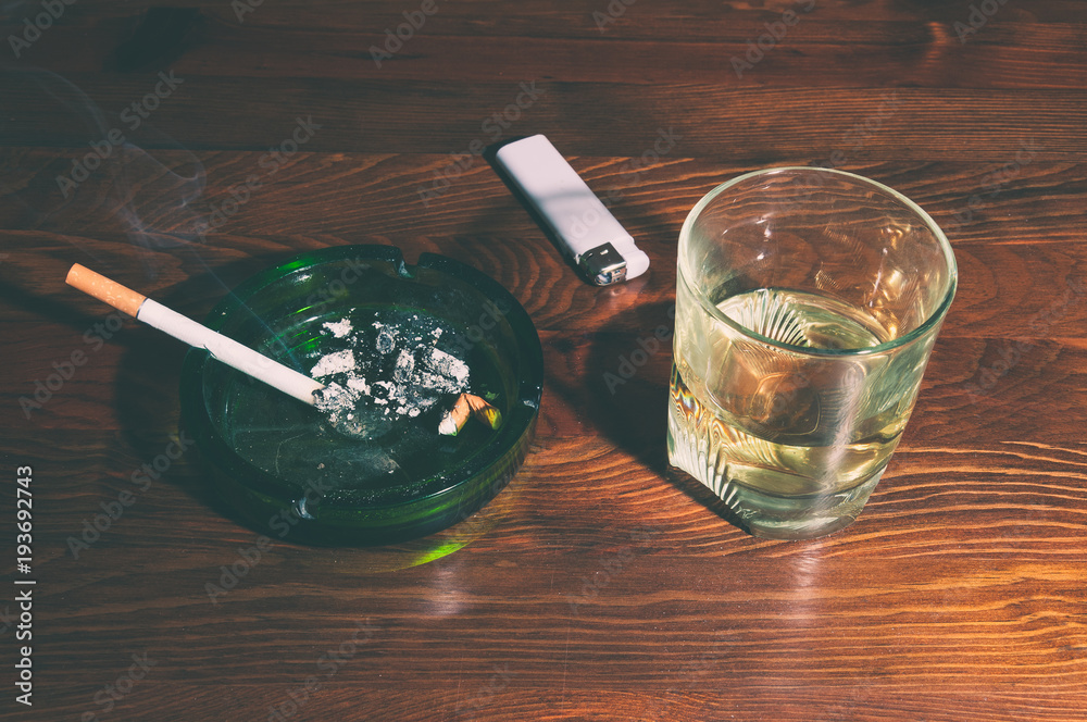liquor and cigarette Smoking cigarette in the ashtray and glass with alcohol drink on the bar  table for addiction concept Stock Photo