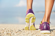 © WHstudio Leushin N - Crropped shot of unrecognizable female in purple sneakers stands on shell beach, wears sport shoes, has morning workout or jogging outdoor, being in movement. Sport and healthy lifestyle concept
