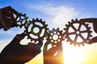 © gerasimov174 - The hands of businessmen connect the gears with a puzzle, against the background of the sun's rays. Business concept, idea, teamwork. Strategy, cooperation, creative.