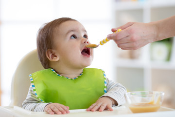 Mum feeds baby boy from a spoon with fruit puree