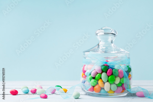 Colorful Candy In Jar Decorated With Bow Ribbon Against Blue