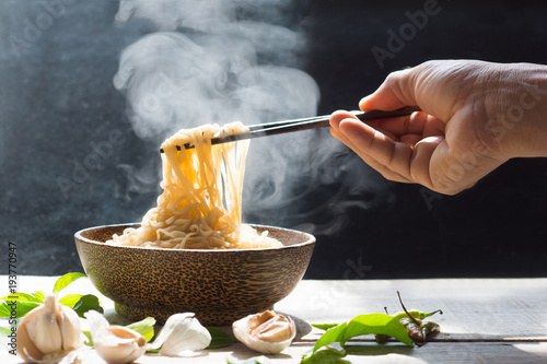 Fotomural Hand uses chopsticks to pickup tasty noodles with steam and smoke in bowl on woo