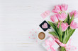 Pink tulips, gift, cup of coffee and paper hearts on white wooden background, copy space and flat lay. Mother's Day concept.