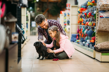 Father and dauther plays with puppy in pet shop