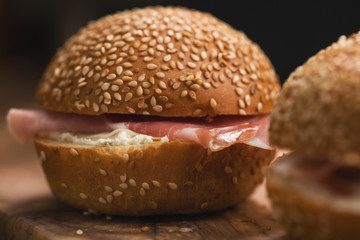 closeup of prosciutto and cream cheese in a sesame buns on wood board