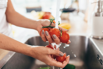 Woman washing tomatoes in kitchen sink close up.