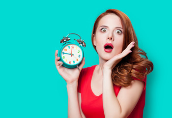 Young beautfiul redhead girl with alarm clock on minty background