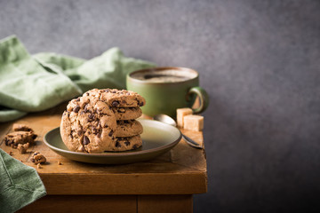 Wall Mural - Stack of chocolate chip cookies on green plate with cup of coffee on old wooden table. Selective focus. Copy space.