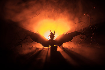 Silhouette of fire breathing dragon with big wings on a dark orange background. Horror image