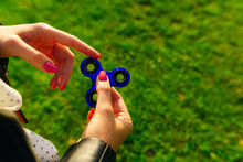 Girl Playing Blue Metal Spinner In Hands On The Street, Female Hands Holding Popular Fidget Spinner Toy On Green Background, Anxiety Relief Toy, Anti Stress And Relaxation Fidgets