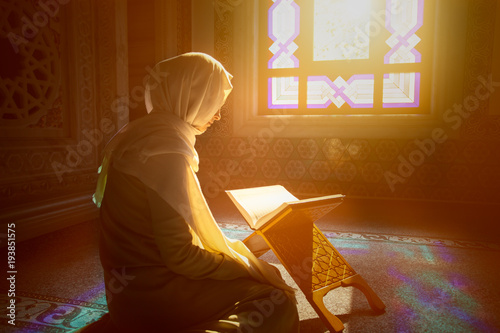 Cuadros en Lienzo Young muslim woman reading Quran in the mosque and sunlight falling from the win