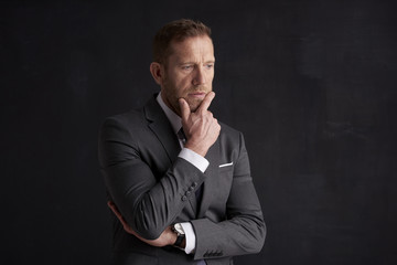 Poster - Nervous, overwhelmed businessman portrait.  Stressed businessman hand is on his forehead while sitting at dark background and thinking very hard. Professional man wearing suit.