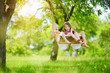 © MNStudio - Two cute little sisters having fun on a swing together in beautiful summer garden on warm and sunny day outdoors