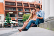 © beatleoff - Young happy couple hugging on the street sitting on the stairs. Smiling man and woman having fun in the city.
