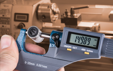 Detail of skilled worker's hand with digital micrometer screw gauge. Accurate measurement of metal linear bearing by measuring tool and lathe in background.