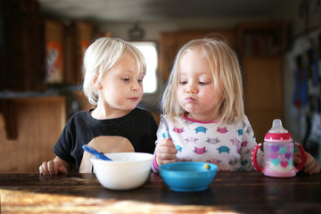 two little toddler girls eating breakfast together