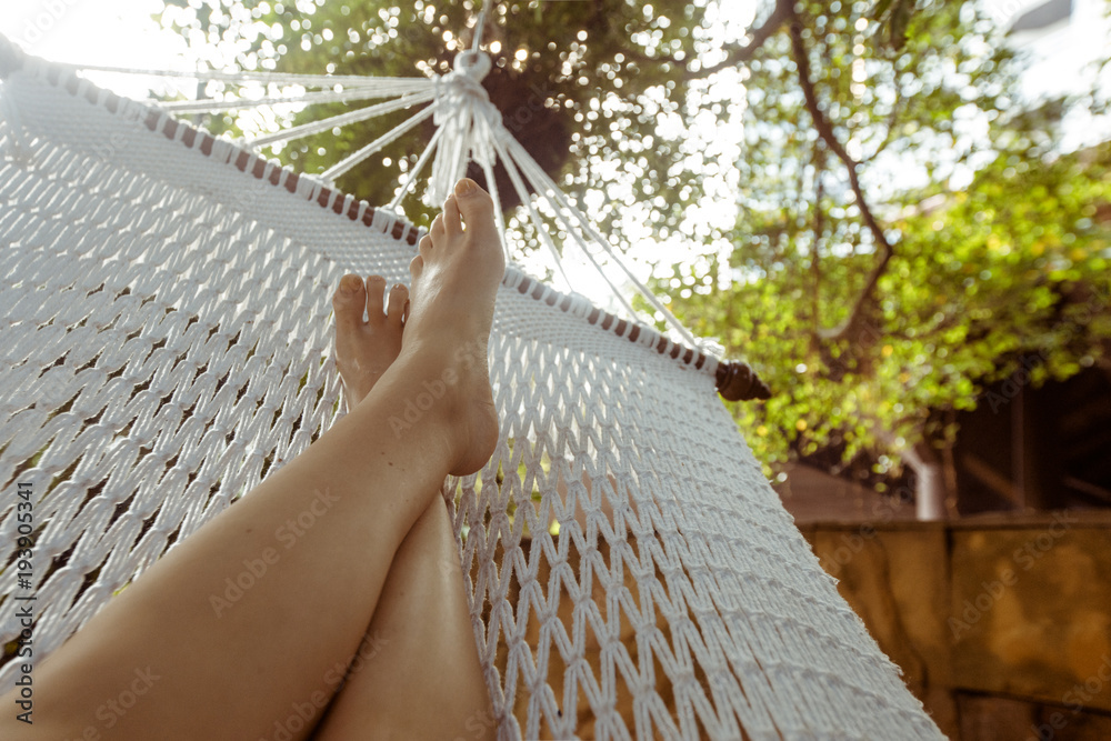Crop shot of barefoot feet lying in white hammock and lounging in backyard. - obrazy, fototapety, plakaty 