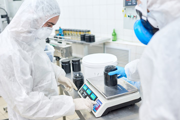 profile view of concentrated factory worker wearing overall and safety mask using electronic scale w