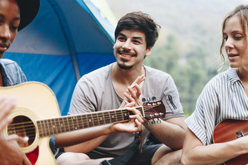 Canvas Print - Group of young adult friends in camp site playing guitar and ukelele and singing together outdoors recreational leisure and friendship concept