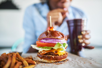 Wall Mural - vegan meatless burger meal with african american woman drinking smoothie in background