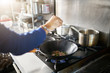 © Joshua Resnick - chef in restaurant kitchen seasoning food in hot skillet wok