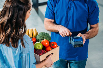 Courier adjusting payment terminal while woman holding groceries in box