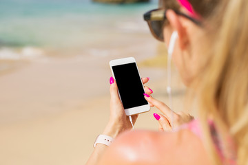 Woman holding mobile phone in hand and listening to music on earbuds
