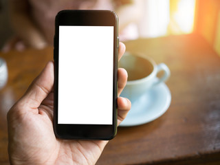 Poster - image of man's hand is holding a black cell phone with blank white screen and blur silver laptop on wood table in coffee cafe  background