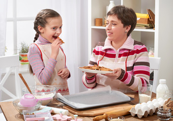 Mother and daughter baking cookies, girl eat cookie, home kitchen interior, healthy food concept