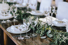 Decorated Elegant Wooden Wedding Table In Rustic Style With Eucalyptus And Flowers, Porcelain Plates, Glasses, Napkins And Cutlery
