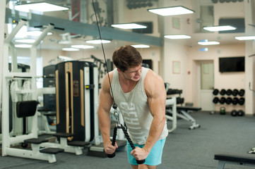 Young sexy male bodybuilder athlete, trains in the gym, using sports equipment and fitness equipment to improving health and beauty of the body