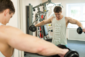 Young sexy male bodybuilder athlete, trains in the gym, using sports equipment and fitness equipment to improving health and beauty of the body