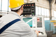 © Seventyfour - Back view of bearded operator wearing protective helmet focused on work while sitting in front of CNC machine, interior of production department on background