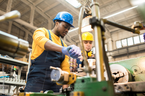Fotomural Multi-ethnic team of workers wearing overalls and protective helmets using lathe