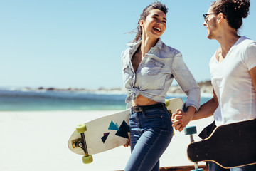 Wall Mural - Smiling couple together at the beach with skateboards