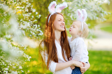 Wall Mural - Young mother and her daughter wearing bunny ears in a spring garden on Easter day