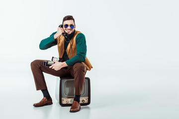 smiling retro styled man sitting on vintage television and talking by stationary telephone