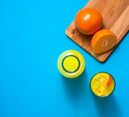 Wall Mural - Glass and bottle of orange juice with half and whole fresh orange fruit on a wooden deck. Turquoise background. Negative space.