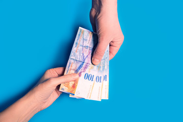 hands passing money, Swiss franc currency on blue background