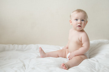 Wall Mural - Beautiful surprised cute blonde baby girl with blue eyes on the bed in the  bedroom. Happy child.  place for text.