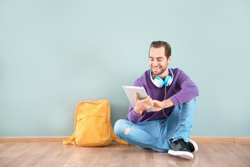 Canvas Print - Student with tablet sitting on floor against color wall