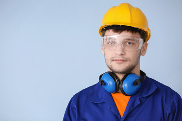 Wall Mural - Male worker with headphones on grey background. Hearing protection equipment