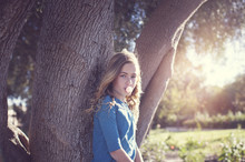 Portrait Of Confident Girl Blowing Bubble Gum Against Tree Trunk At Park