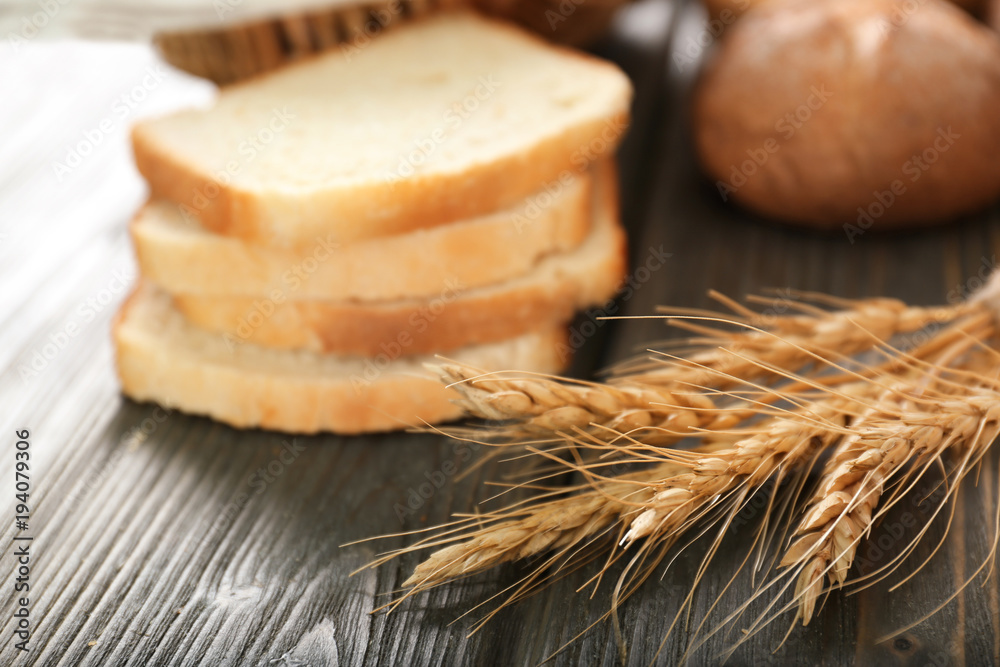 Wheat spikes and cut bread on table