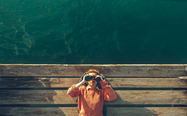 young beautiful girl lies on a pier near the sea and looks through binoculars on the sky. travel sea