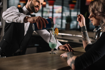 Wall Mural - smiling handsome bartender preparing alcohol cocktail for girl